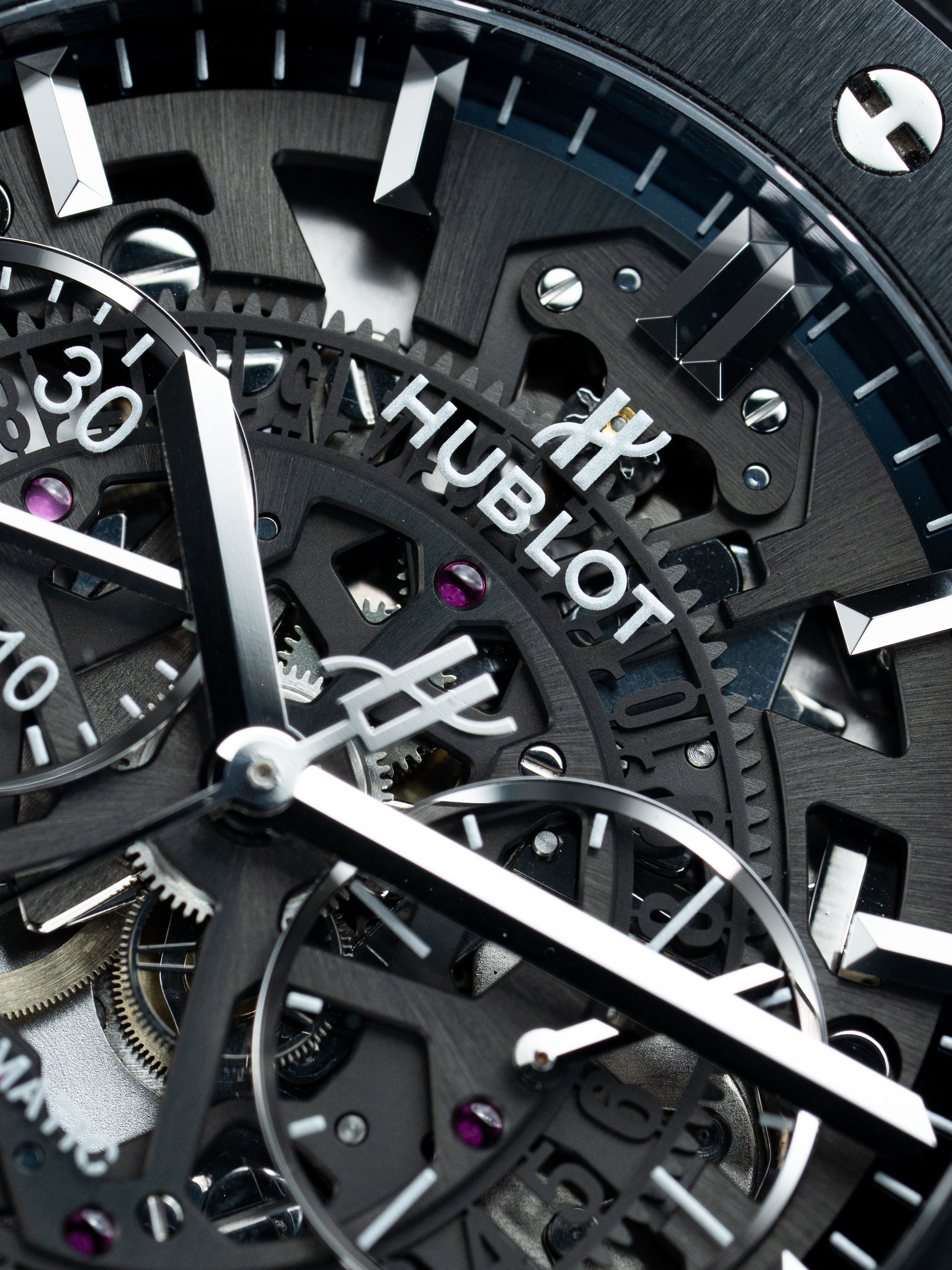 Extreme close-up of a Hublot watch dial showing indices, hands, and texture in low light